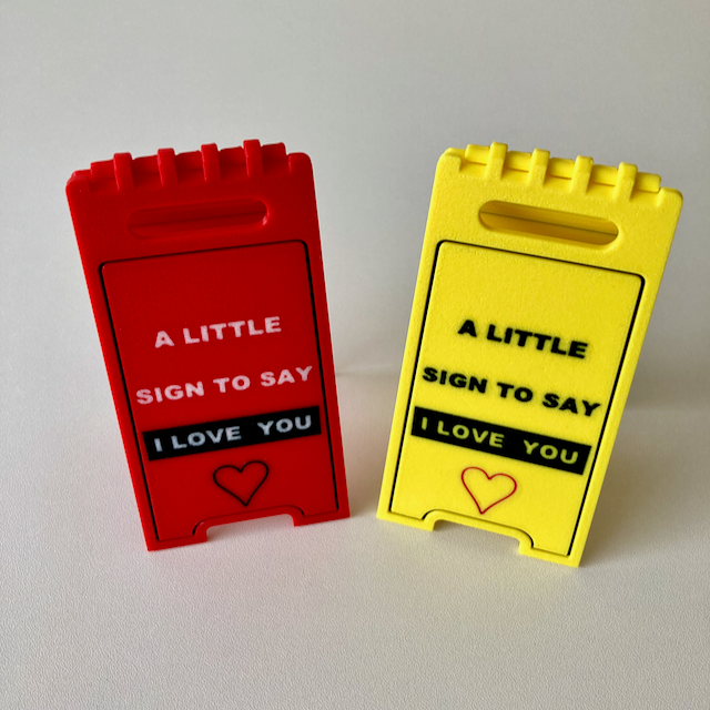 Two 3D printed small hinged red and yellow Valentine's Day decorative signs with the phrase 'A LITTLE SIGN TO SAY I LOVE YOU'.