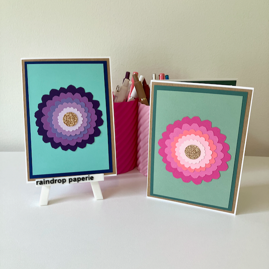 Two handmade greeting cards with large zinnia flowers and glitter centers.