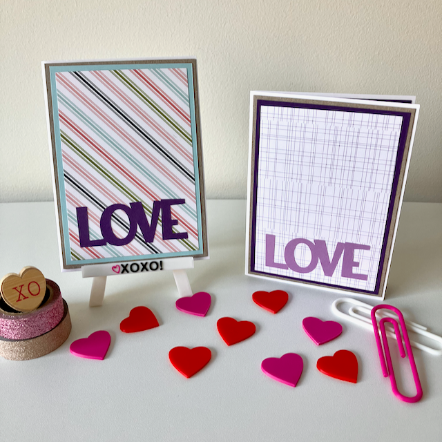 Two handmade greeting cards with 'love' text displayed on a desk with decorative hearts and a stamp.