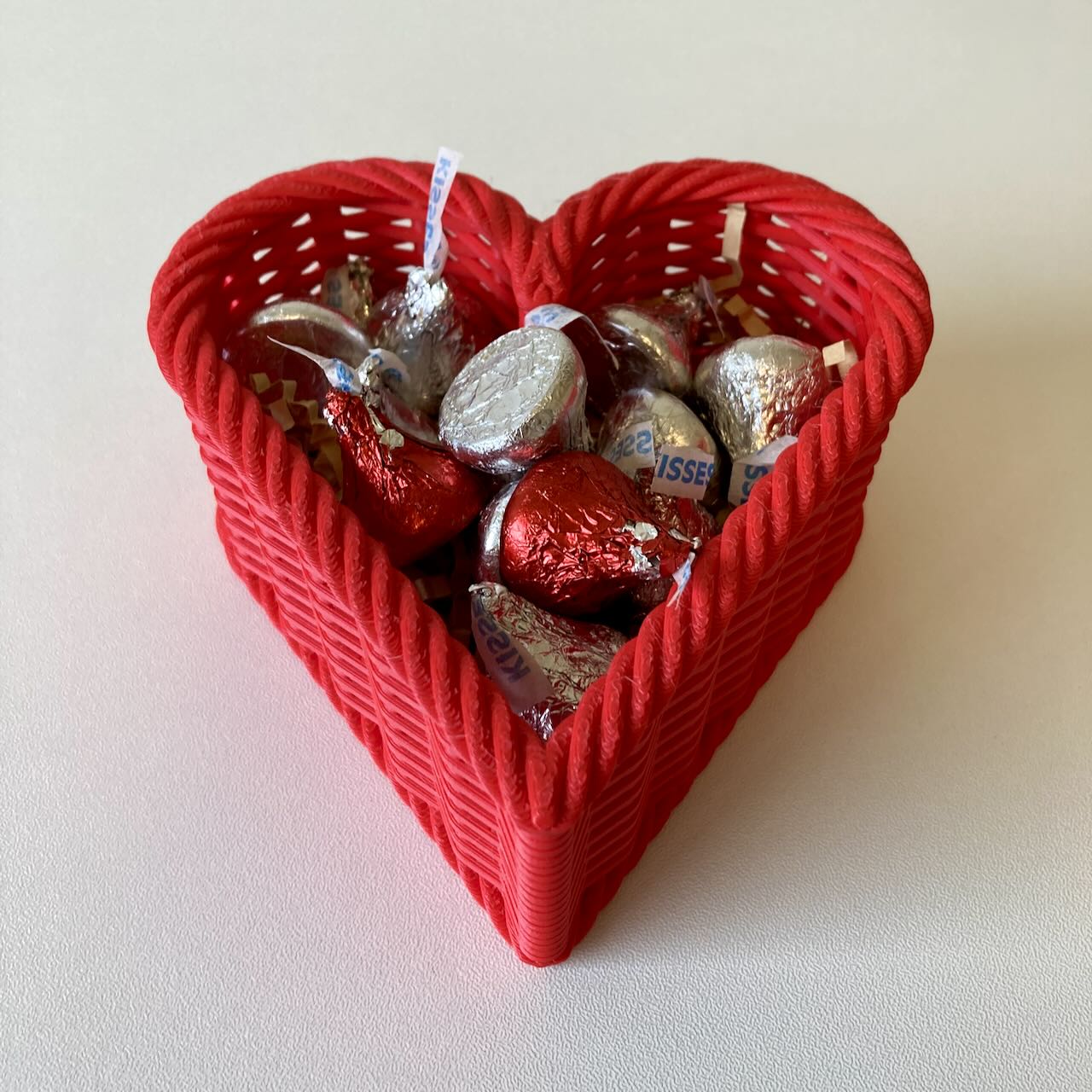 A 3D printed red woven heart shaped basket as a Valentine's Day decoration with candy in it.