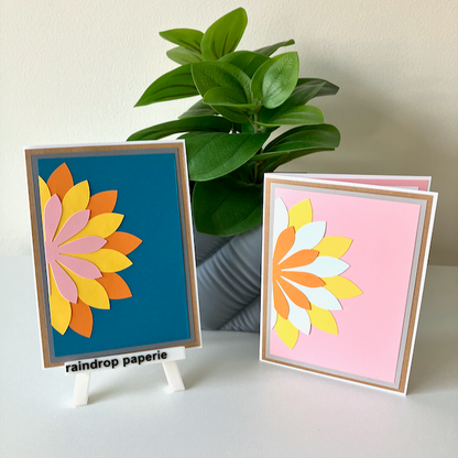 Two handmade greeting cards with a floral design, displayed on a table with a plant in the background.