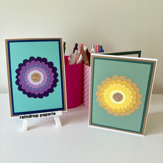 Two handmade greeting cards with large zinnia flowers and glitter centers.