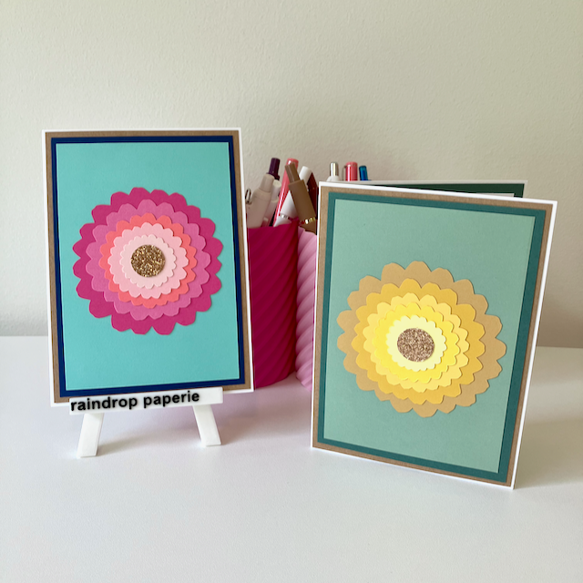 Two handmade greeting cards with large zinnia flowers and glitter centers.
