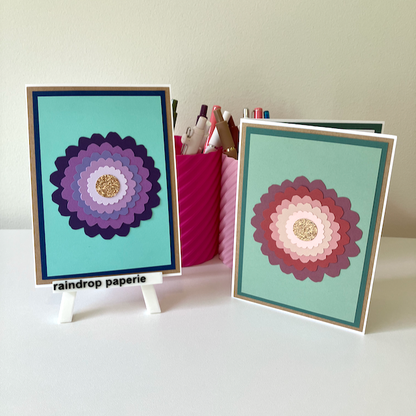 Two handmade greeting cards with large zinnia flowers and glitter centers.