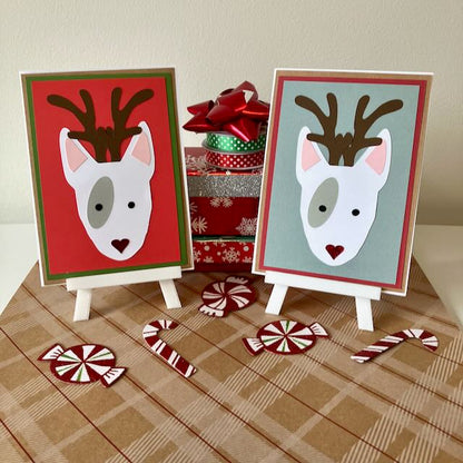 Two Christmas-themed cards with reindeer designs on small easels, surrounded by candy canes and a gift box.