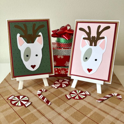 Two greeting cards bull terrier reindeer on easels with Christmas decorations in the background.