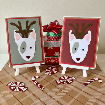 Two handmade Christmas-themed greeting cards with English bull terriers as reindeers on little stands, surrounded by candy canes and gift boxes.