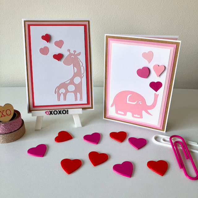 Two handmade greeting cards with animal and heart decorations displayed on a table with heart-shaped decorations.