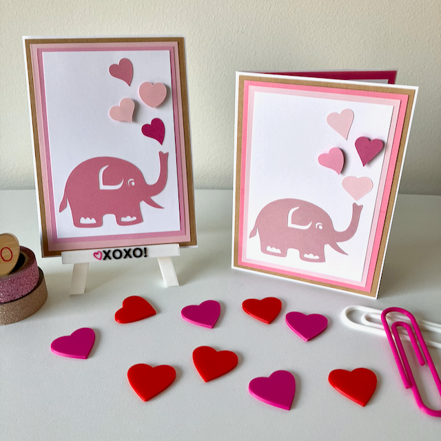 Two handmade greeting cards with animal and heart decorations displayed on a table with heart-shaped decorations.