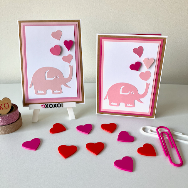 Two handmade greeting cards with animal and heart decorations displayed on a table with heart-shaped decorations.