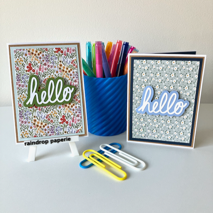 A set of handmade greeting cards with 'Hello' text, accompanied by floral designs, displayed on a white surface.