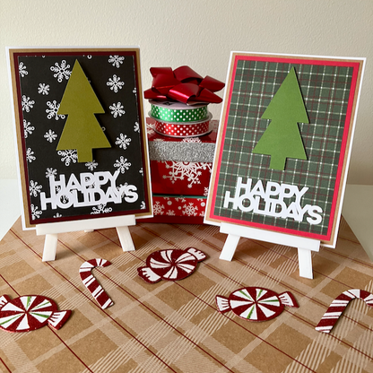 Two 'Happy Holidays' greeting cards with Christmas tree designs on a checkered surface with candy decorations.