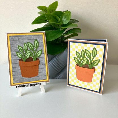Two handmade greeting cards with a garden pot and green foliage displayed on a table. 