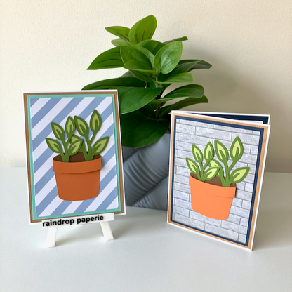 Two handmade greeting cards with a garden pot and green foliage displayed on a table. 