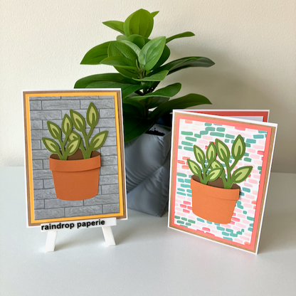 Two handmade greeting cards with a garden pot and green foliage displayed on a table. 