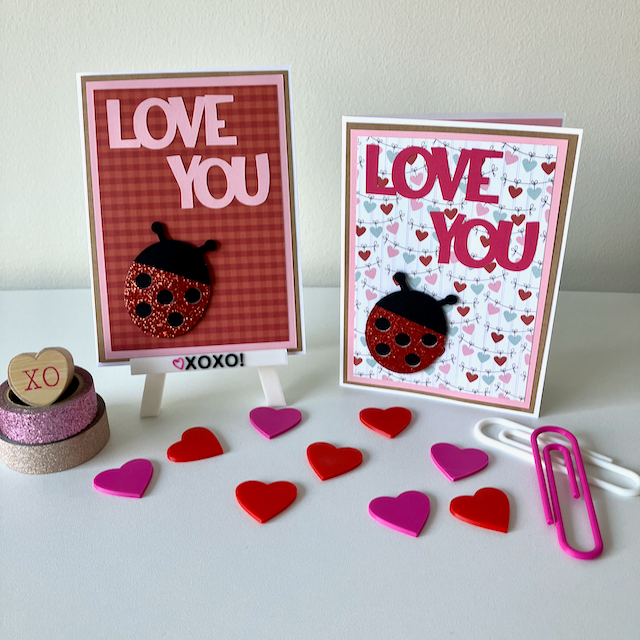 Two handmade greeting cards with lady bugs and 'love you' text displayed on a table with decorative hearts. 