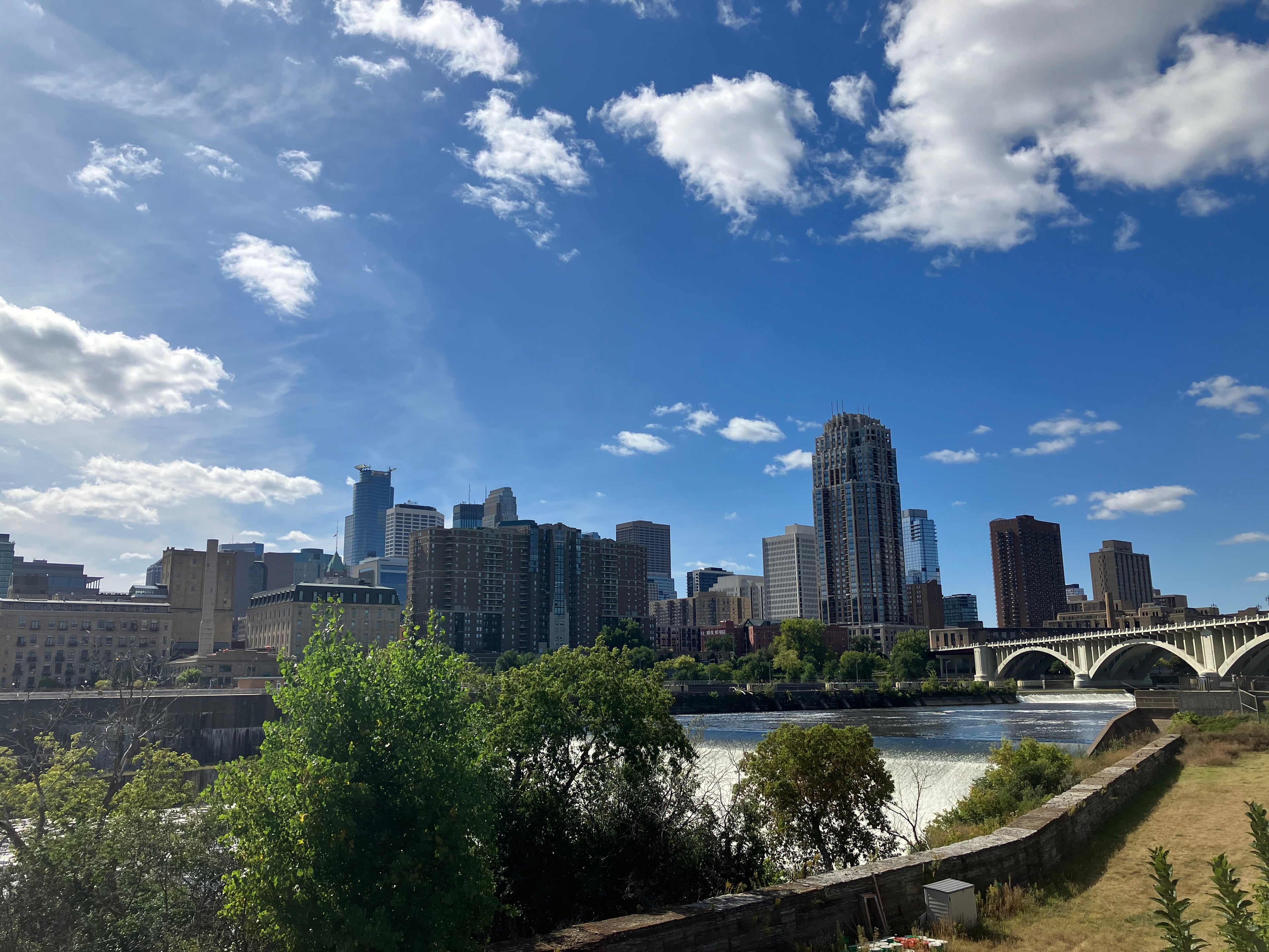 Minneapolis skyline with skyscrapers, a river, bridge and a blue sky with clouds.