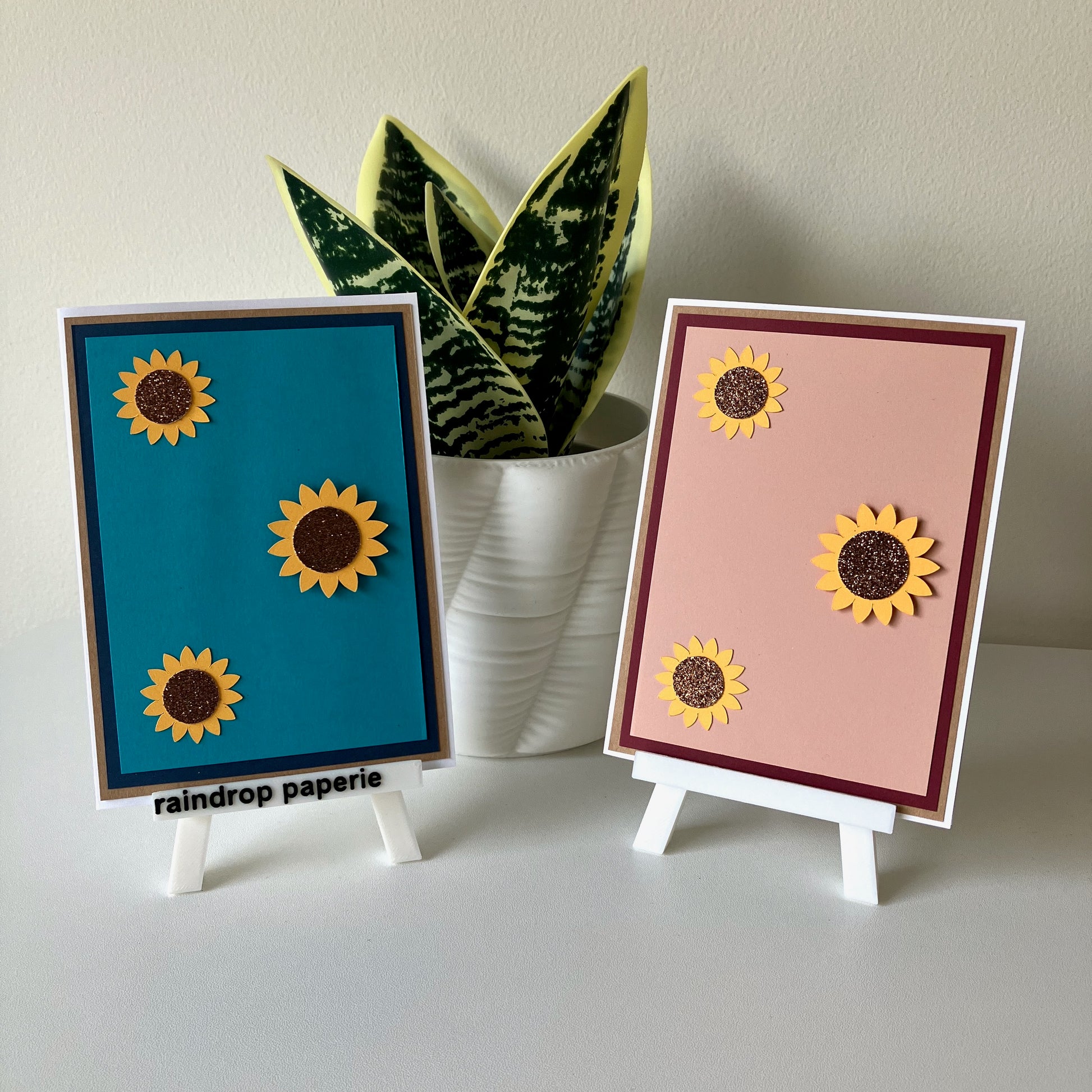 Two sunflower-themed cards on small stands with a plant in the background.