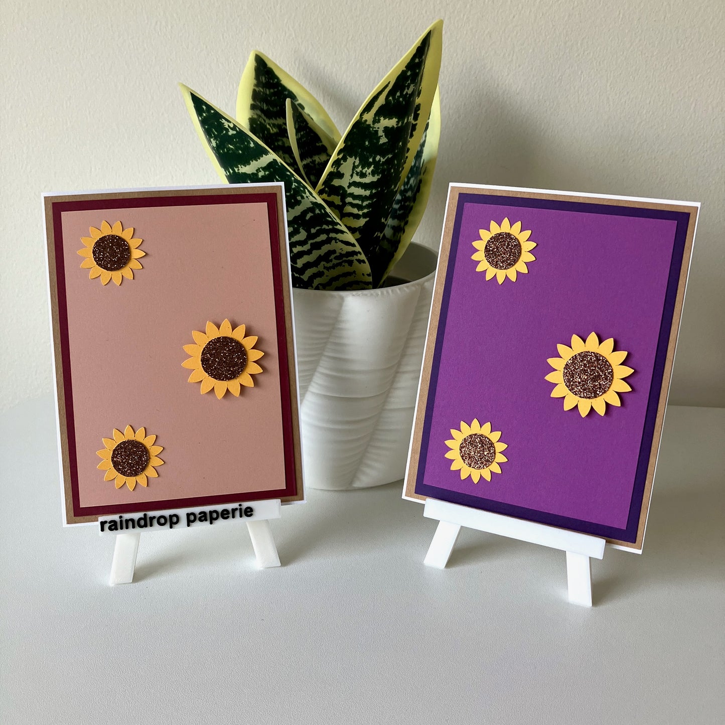 Two sunflower-themed cards on small stands with a plant in the background.