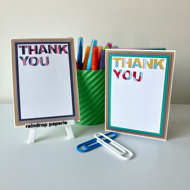 Two 'Thank You' cards with a green cup of colorful markers on a white surface.